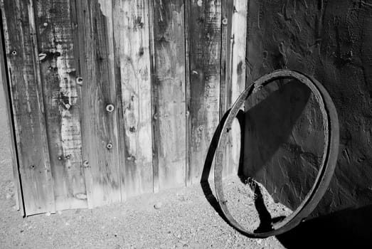 Black and white of Old iron and wood wagon wheel against and old wooden and adobe wall.