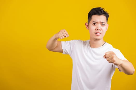 Asian handsome young angry man showing punch a clenches fist, aggressive male punching towards the camera looking to camera, studio shot isolated on yellow background
