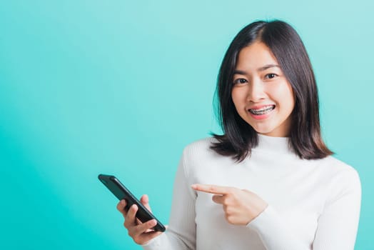 Portrait of Asian woman smile she holding and typing text message on a smartphone, female excited cheerful her reading mobile phone some social media isolated on a blue background, Technology concept