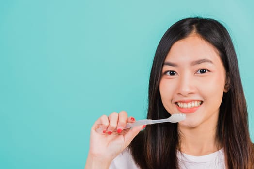 Asian beautiful young woman teen brushing teeth in the morning, portrait of happy Thai female confident smiling holding toothbrush, studio shot isolated on blue background, Dental health concept