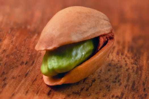 Shallow depth of field (extreme close up) single pistachio in shell, green nut visible, on wooden board.