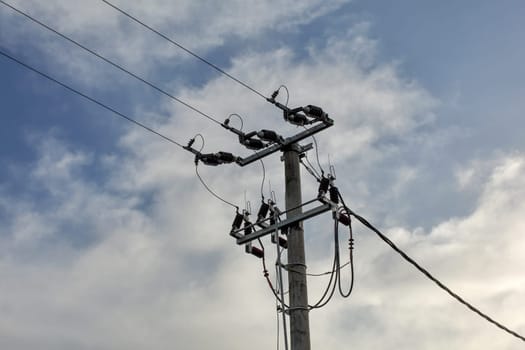 Small concrete pillar with power lines, sky with clouds in background.