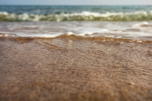 Very low angle (camera on ground, close up) sea water washing the sand. Selective focus on the wet beach, abstract summer holiday / vacation background.