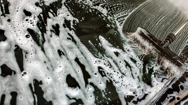 Widshield of a car being washed in self serve carwash, brush leaving strokes in white shampoo and foam on glass.