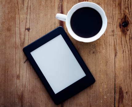 E-book reader and coffee cup on wooden table