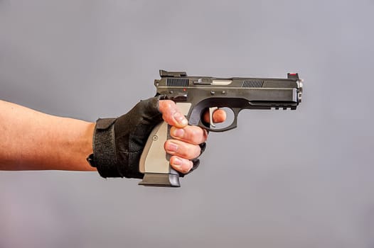 A man's hand holds a black pistol in his hand on a gray background. High quality photo