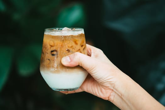 Hand hold iced latte coffee in a glass with cream on bottom . cold summer drink background