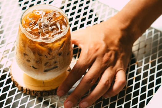 Hand hold iced latte coffee in a glass with cream on bottom . cold summer drink background