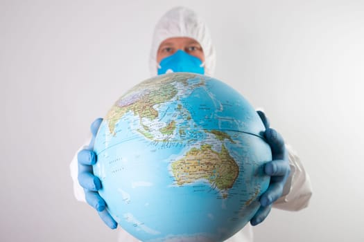World epidemic danger concept. Male doctor man in medical face mask and gloves protecting planet Earth.