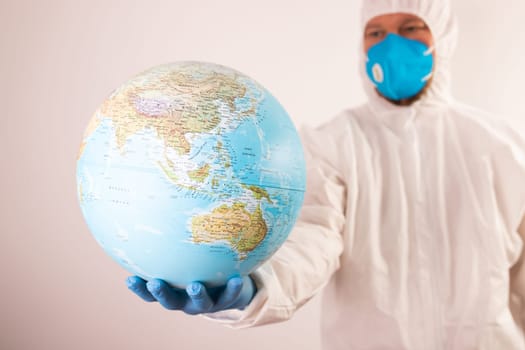 World epidemic danger concept. Male doctor man in medical face mask and gloves protecting planet Earth.