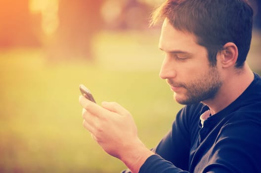 Young man sitting in the park and texting a message