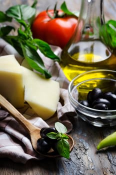 Cheese, olives, basil, tomato and olive oil on wooden table