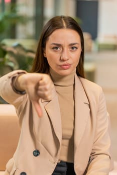 Dislike. Upset Caucasian businesswoman sitting in office lobby showing thumb down sign gesture, expressing discontent, disapproval dissatisfied bad work. Displeased serious freelancer in formals.