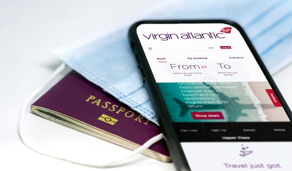 London, UK, July 2021: phone with the Virgin Atlantic airlines app on the screen lying over a protective mask and a passport. Travel safety and restrictions during coronavirus pandemic