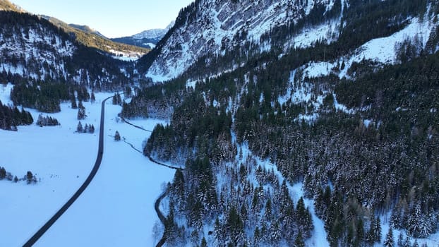 Aerial drone shot of snowy landscape with road and mountain forest