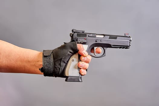A man's hand holds a black pistol in his hand on a gray background. High quality photo