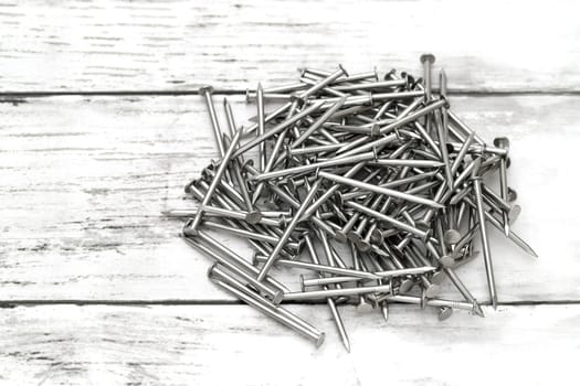 Pile of silver metallic nails on white wooden background