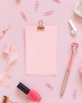 Paper with a clip and Pink school accessories on pastel pink, top view, textbook mockup. Girly workplace with scissors, pencils, pen, paperclips, earrings and watch. Back to school concept
