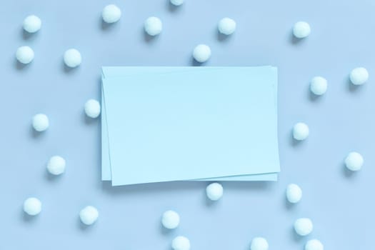 Blank card between pastel pom-poms on light blue top view. Romantic scene with blank horizontal card with place for text flat lay. Spring or boyish concept