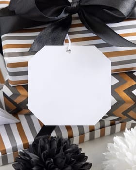 Present with blank gift tag and black bow close up. Gift boxes wrapped in Striped and chevron geometric paper near black and white decor. Christmas, New Year, Birthday, Anniversary label mockup