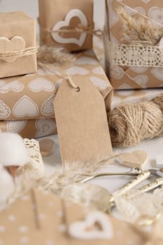 Valentines wrapped presents with vertical gift tag close up. Spring scene with blank label. Rustic, cottage chic or bohemian mockup, copy space