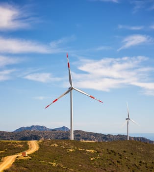 Wind turbines on a beautiful blue sky with clouds in a mountain wind farm in Sardinia. Renewable energy concept, green energy generation. Energy industry.