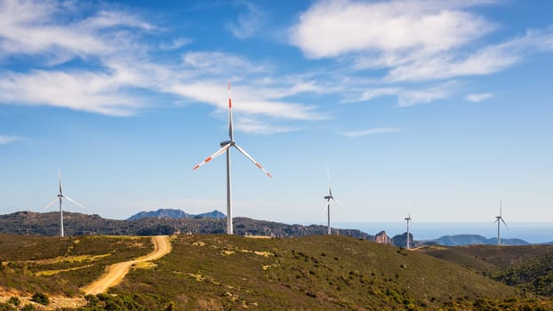 Wind turbines on a beautiful blue sky with clouds in a mountain wind farm in Sardinia. Renewable energy concept, green energy generation. Energy industry.