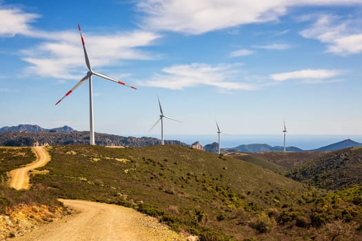 Wind turbines on a beautiful blue sky with clouds in a mountain wind farm in Sardinia. Renewable energy concept, green energy generation. Energy industry.