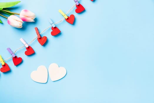 Valentine's day concept. red heart-shaped valentines decoration hanging with wood clips for happy love on the rope and white heart greeting card isolated on blue background with copy space