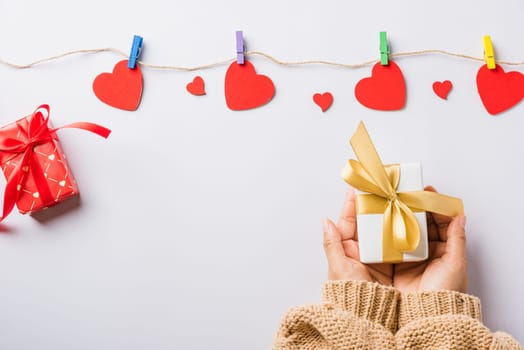 Valentine's day and birthday. Woman hands holding gift or present box decorated and red heart surprise on white background, Female's hand hold gift box package in craft paper Top view flat lay
