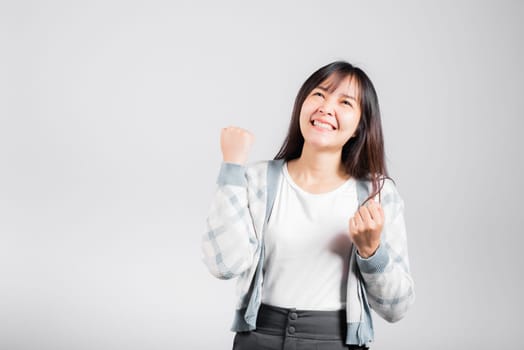 Smiling happy woman makes raised fists up celebrating her winning success gesture, Happy Asian beautiful young female excited say yes, studio shot isolated on white background with copy space