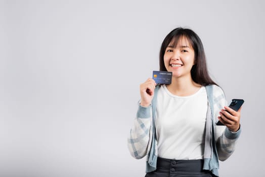 Woman excited smiling hold mobile phone and plastic debit credit bank card for payment studio shot isolated white background, happy young female using smartphone buy and pay online shopping