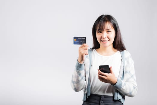 Woman excited smiling hold mobile phone and plastic debit credit bank card for payment studio shot isolated white background, happy young female using smartphone buy and pay online shopping