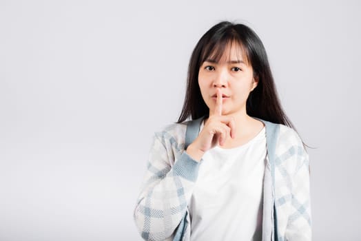 Woman making finger on lips mouth silent quiet gesture, Happy Asian beautiful young female marking silencefor stop quiet, mute studio shot isolated on white background with copy space