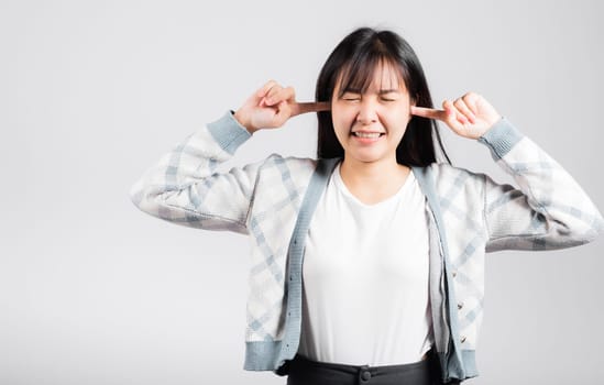 Woman bad mood pain her closed ears with finger and close eyes, Asian beautiful young female covers ears for loud noise, studio shot isolated on white background with copy space