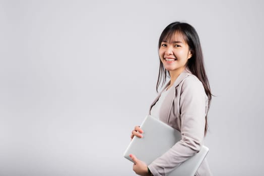 Side view woman smiling confident smiling holding closed laptop, Portrait excited happy Asian young female person hugging close cover computer device studio shot isolated on white background