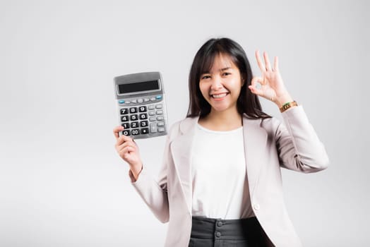 Tax day concept. Woman confident smiling holding electronic calculator and show OK gesture, excited happy Asian female studio shot isolated on white background, Account and finance counting income