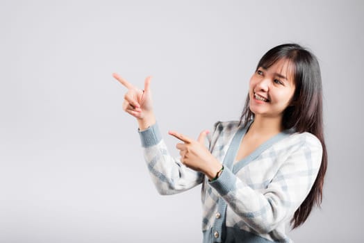 Smiling happy woman pointing finger out space, Portrait Asian beautiful young female point into empty looking to side away, studio shot isolated on white background with copy space