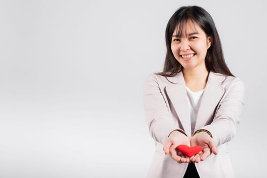Smiling woman confidence showing holding red heart with her hand palm isolated white background, Asian happy portrait beautiful young female send love and happy valentine in studio shot, copy space