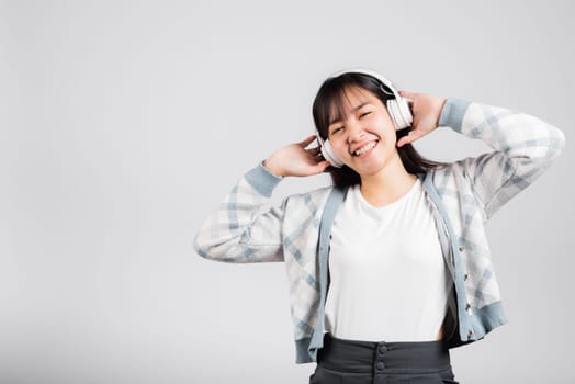 Woman excited smiling listening to music radio in bluetooth headphones and holding phone studio shot isolated white background, happy Asian young female listen modern technology mobile phone
