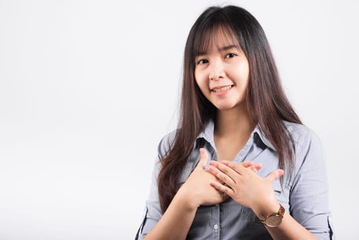 Happy woman in casual clothes holding hands at chest close to heart meditating and smiling in studio short isolated on white background, believe faith and love gratitude concept