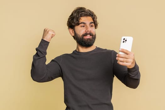 Happy excited joyful Lebanese man in long sleeves using smartphone typing browsing shouting say wow yes found out great big win, good news, lottery goal achievement, celebrating success, winning game.