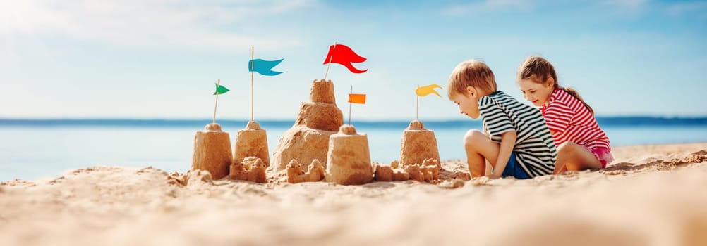 Boy and girl playing on the beach on summer holidays. Children building a sandcastle at the sea.