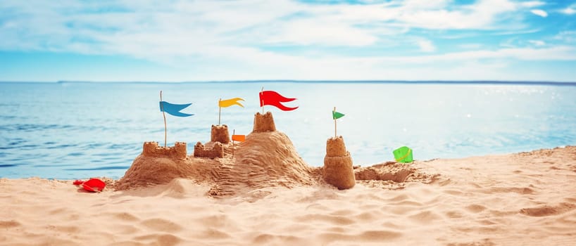 Sand castle with colourful flags on the beach of the sea. Panoramic view. Concept of the vacation and tourism.
