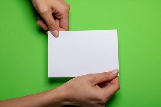 two female hands holding a blank piece of paper with copy space in front of a green colored background cardboard