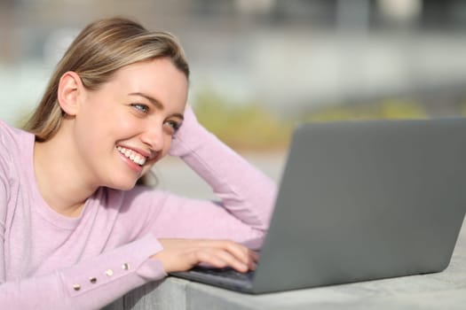 Happy teen using laptop sitting in the street