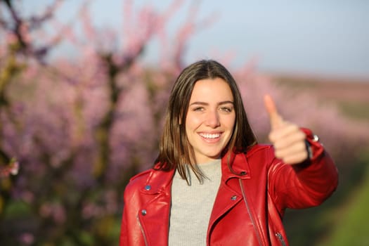 Happy woman in red gesturing thumb up in a field