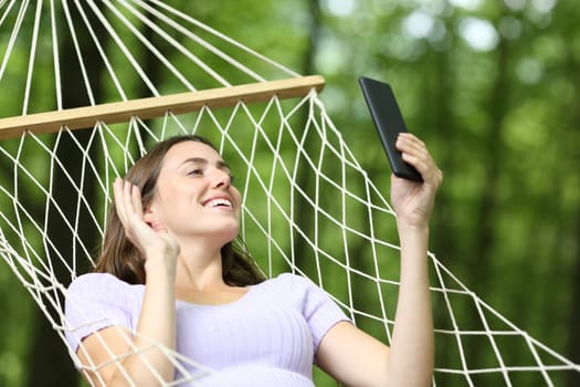 Happy woman having videocall on phone on hammock