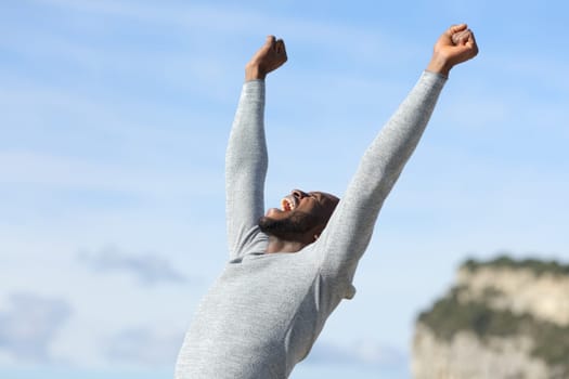 Euphoric man with black skin raising arms in nature