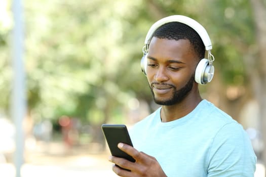 Man with black skin listening to music with phone in park